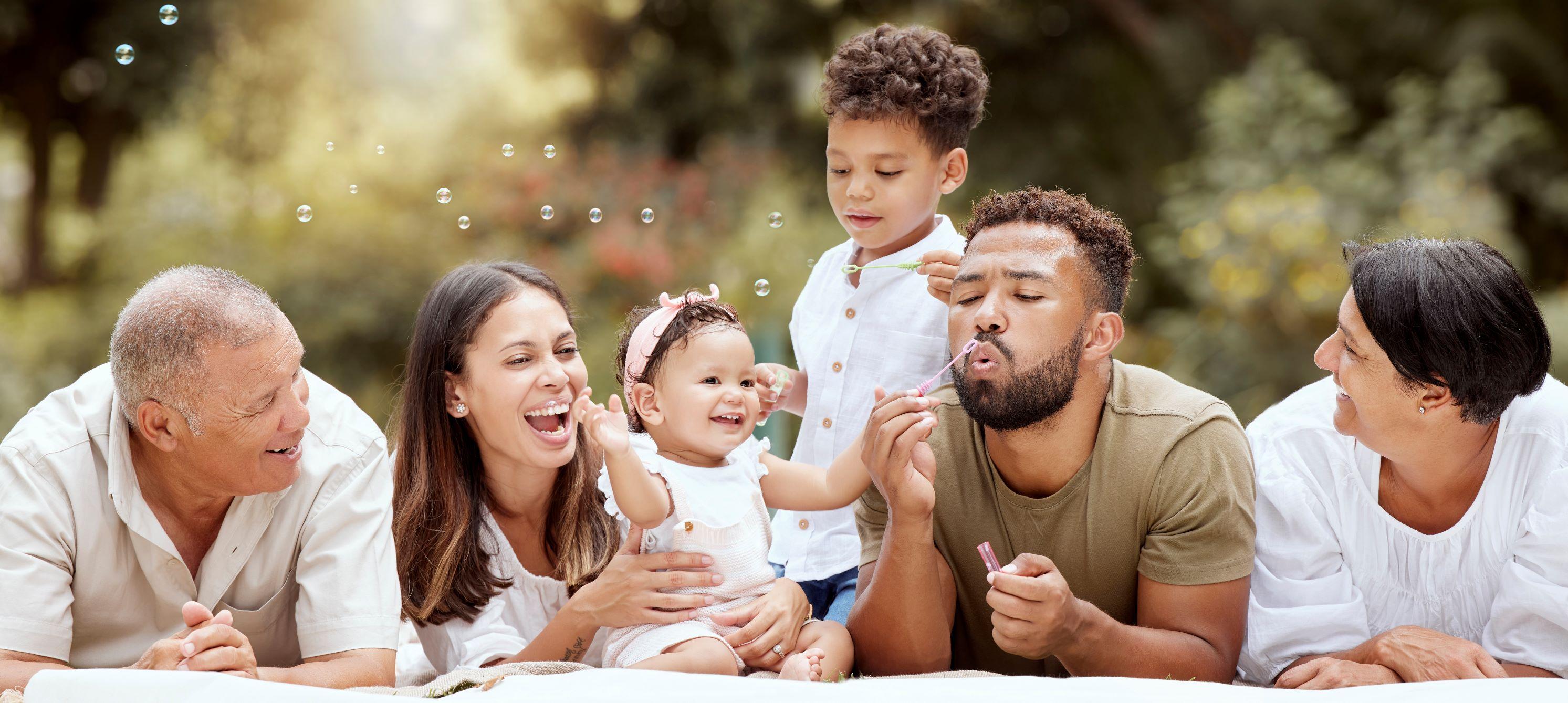 A family of varying ages and genders all laid on the ground outside with a baby and a young child.