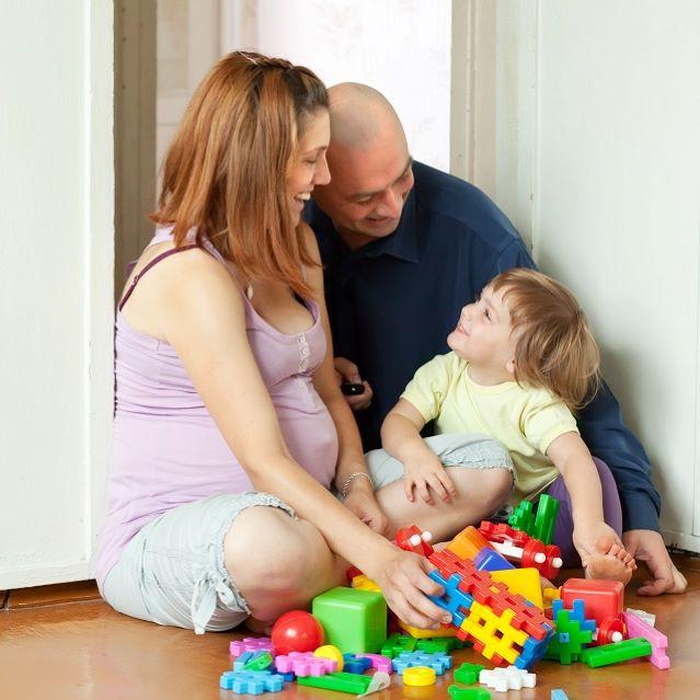 A man and a pregnant woman sat on the floor playing with bricks with a small child.