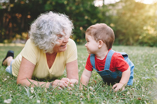 An older woman on the grass with a small child, facing each other and talking