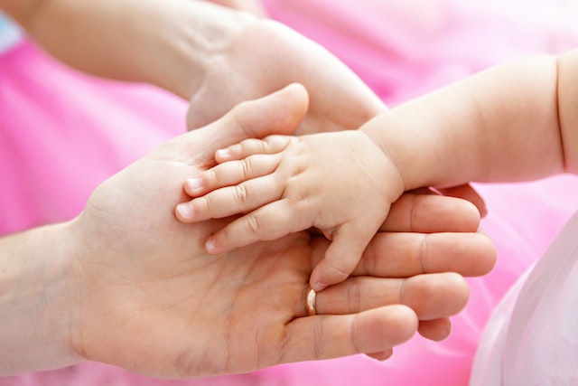 A baby&#039;s hand resting on the hand of two adults